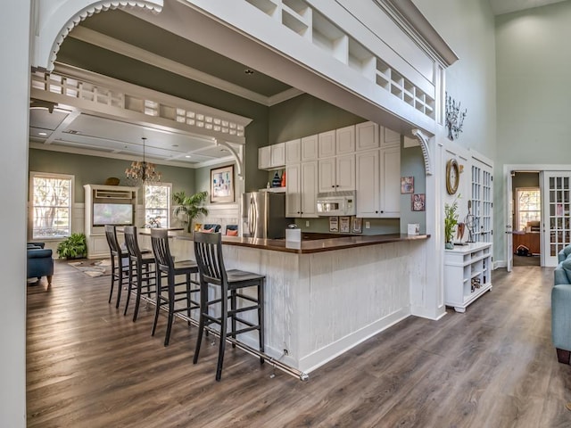 kitchen with a breakfast bar, hanging light fixtures, ornamental molding, stainless steel fridge with ice dispenser, and kitchen peninsula