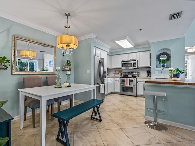 kitchen with crown molding, appliances with stainless steel finishes, butcher block counters, white cabinetry, and decorative light fixtures