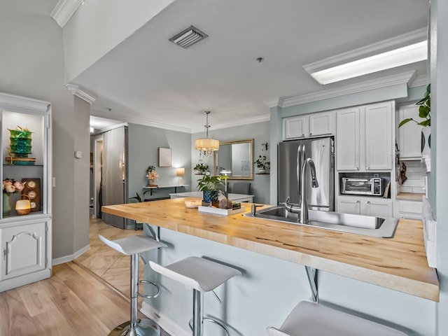 kitchen featuring butcher block countertops, a breakfast bar area, stainless steel fridge, white cabinets, and hanging light fixtures