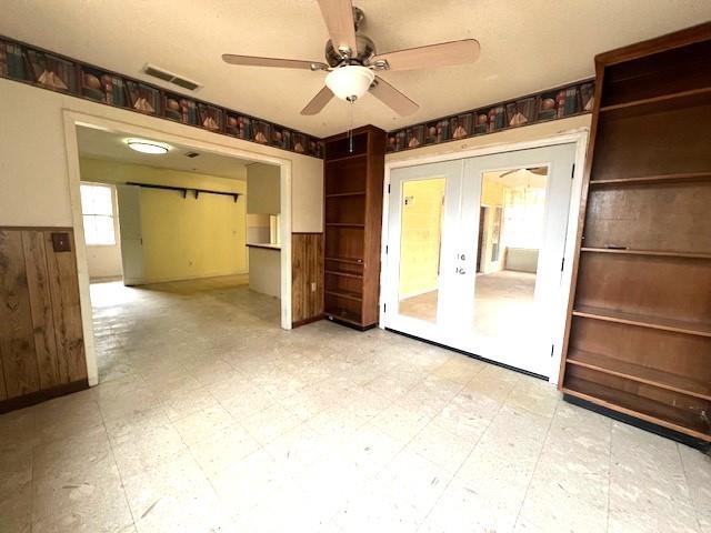 unfurnished living room with ceiling fan, wooden walls, and french doors