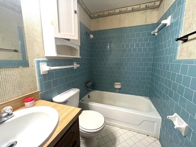 full bathroom with tile walls, vanity, tiled shower / bath combo, and toilet