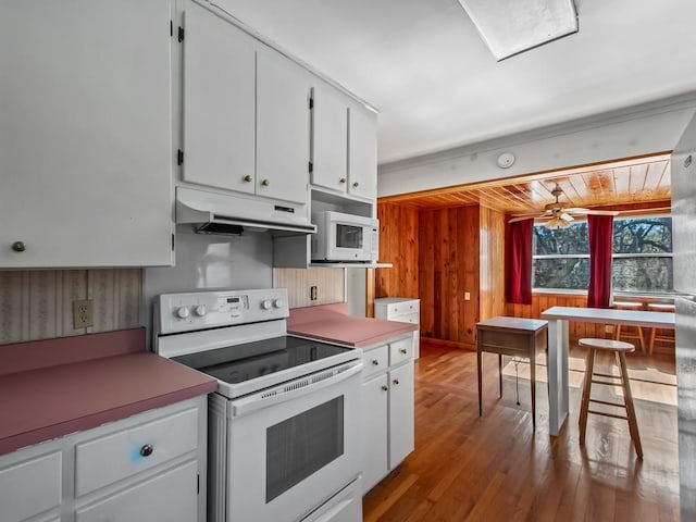 kitchen with white appliances, ceiling fan, white cabinetry, light hardwood / wood-style floors, and wood walls