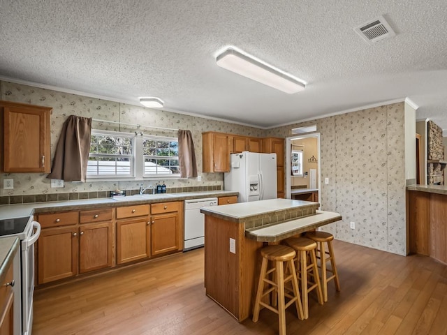 kitchen featuring white appliances, a breakfast bar, a kitchen island, and light hardwood / wood-style flooring