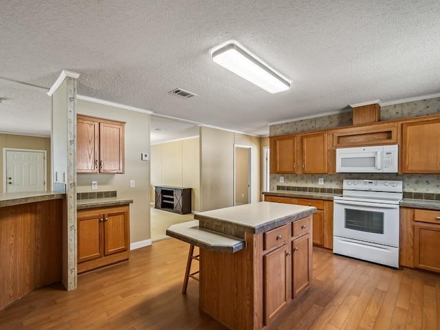 kitchen featuring wood-type flooring, a kitchen island, a breakfast bar area, and white appliances