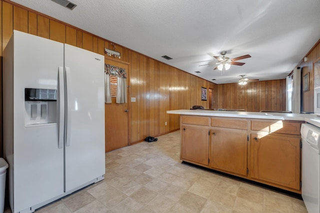 kitchen featuring kitchen peninsula, wooden walls, ceiling fan, white appliances, and a textured ceiling