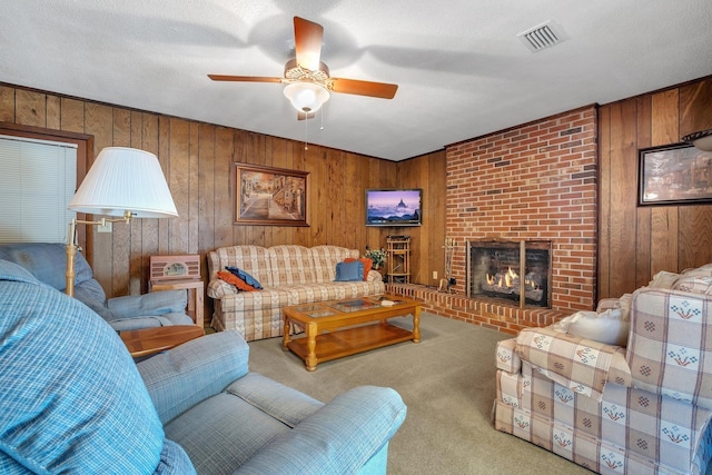 living room with ceiling fan, a fireplace, wood walls, carpet flooring, and a textured ceiling