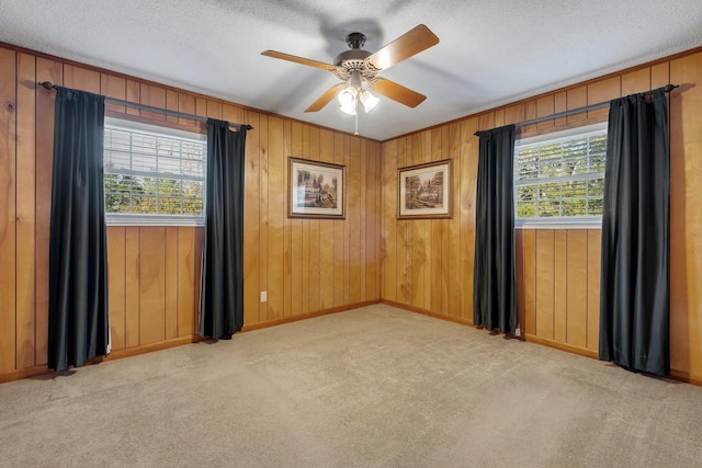 spare room with ceiling fan, light colored carpet, a textured ceiling, and wood walls