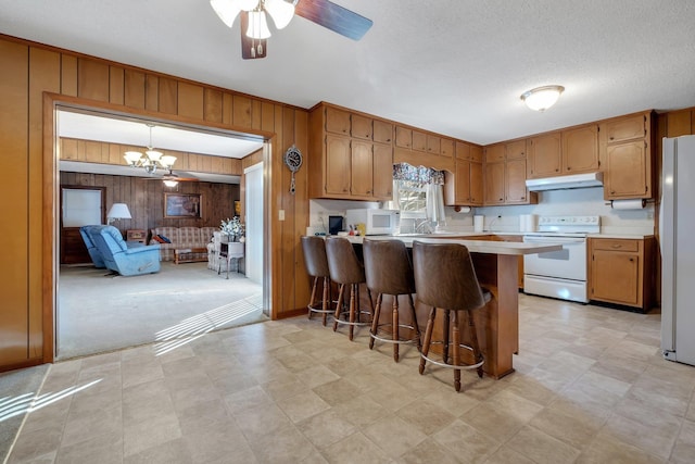 kitchen featuring kitchen peninsula, wood walls, a breakfast bar area, white appliances, and pendant lighting