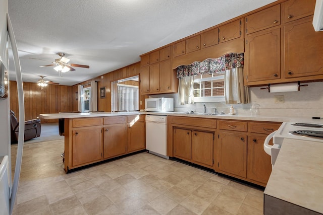 kitchen featuring a textured ceiling, white appliances, wooden walls, kitchen peninsula, and ceiling fan