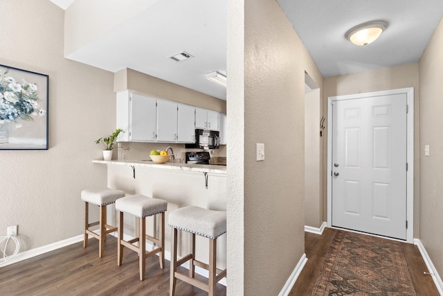 kitchen featuring electric stove, a breakfast bar area, white cabinetry, dark hardwood / wood-style floors, and kitchen peninsula