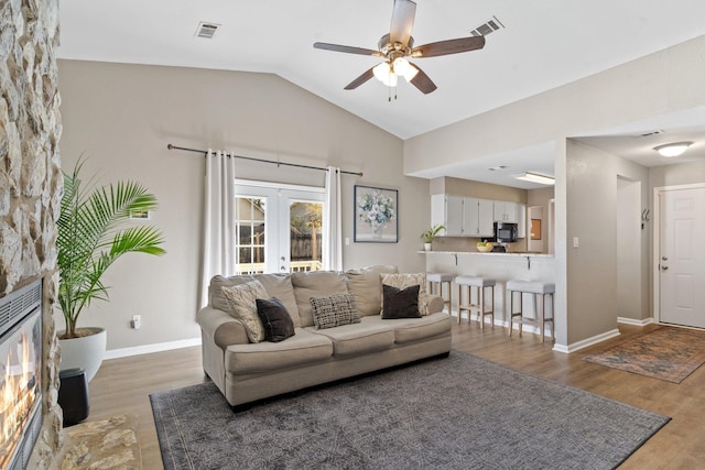 living room featuring french doors, vaulted ceiling, hardwood / wood-style flooring, ceiling fan, and a fireplace