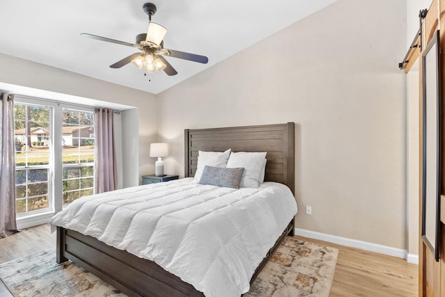 bedroom with lofted ceiling, a barn door, ceiling fan, and light wood-type flooring