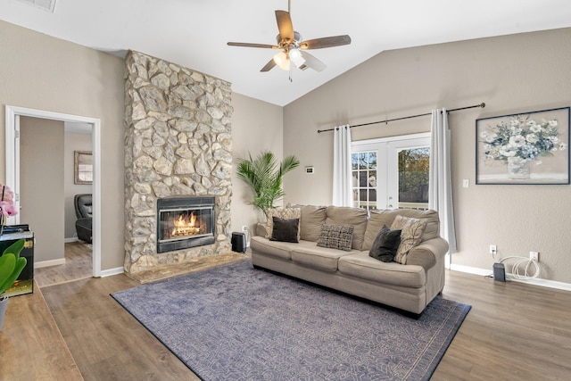 living room with hardwood / wood-style flooring, ceiling fan, a stone fireplace, vaulted ceiling, and french doors