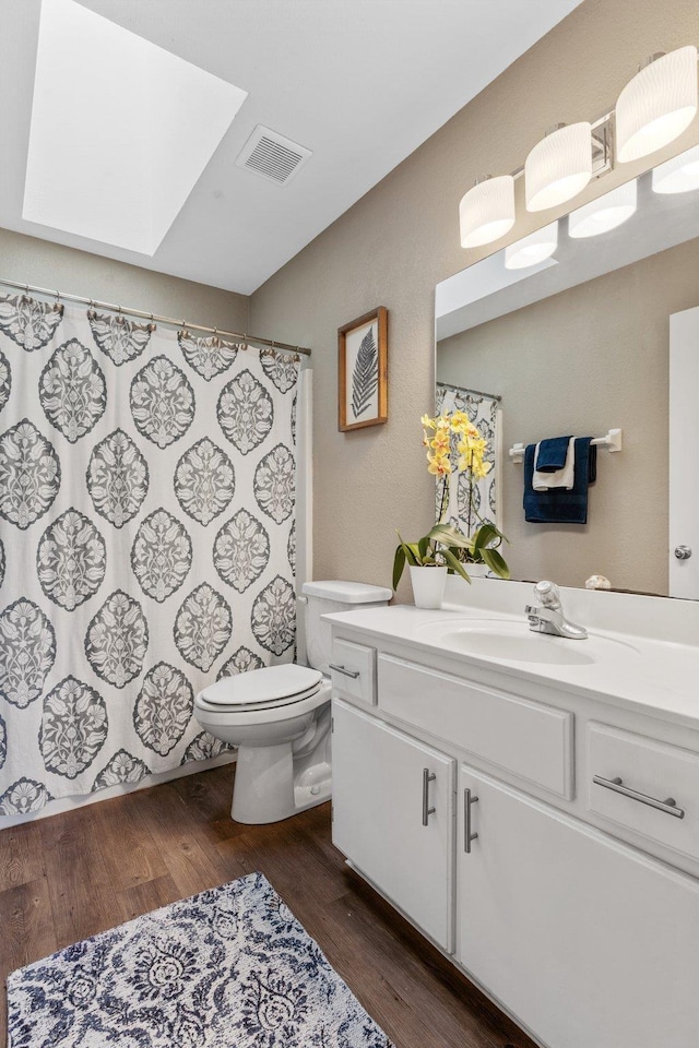 bathroom featuring wood-type flooring, toilet, a skylight, and vanity