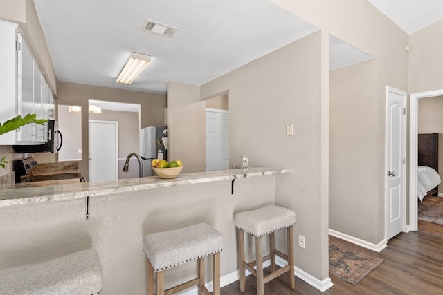 kitchen featuring white cabinetry, stainless steel appliances, a kitchen breakfast bar, light stone counters, and dark hardwood / wood-style flooring