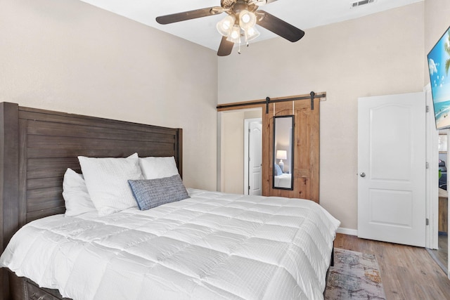 bedroom featuring ceiling fan, a barn door, and light hardwood / wood-style floors