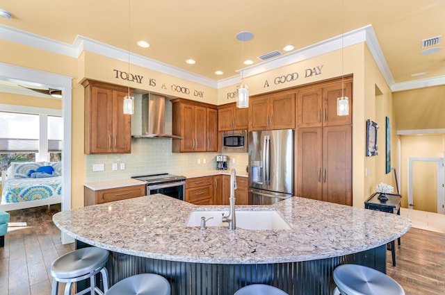 kitchen featuring pendant lighting, a spacious island, wall chimney range hood, appliances with stainless steel finishes, and a breakfast bar area