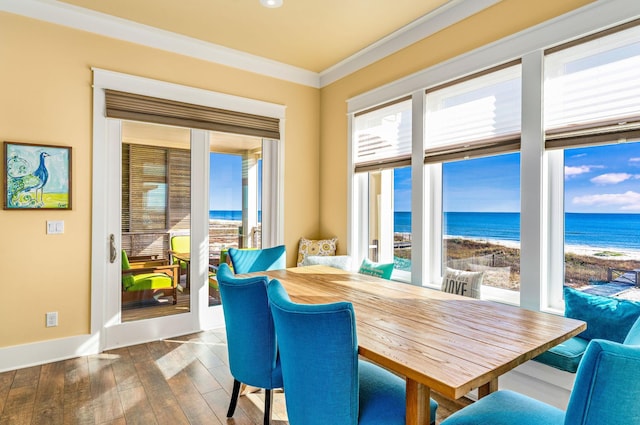 dining space featuring dark hardwood / wood-style flooring, a water view, a view of the beach, and ornamental molding