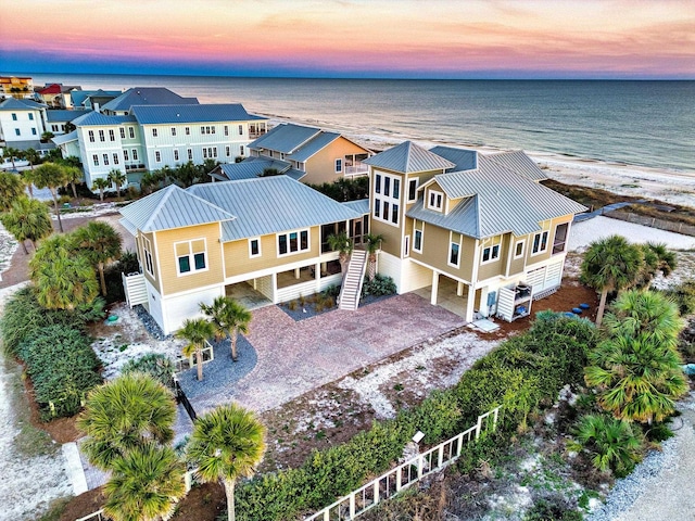 aerial view at dusk featuring a water view and a beach view