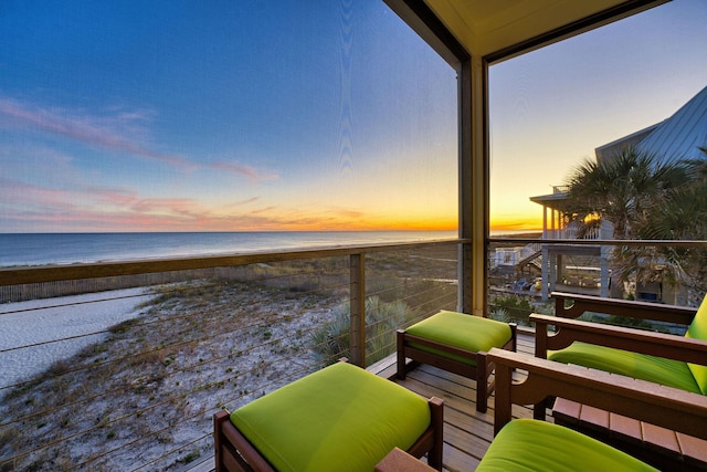 balcony at dusk featuring a water view and a beach view