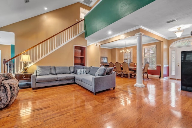 living room featuring wood-type flooring, ornate columns, crown molding, and a notable chandelier