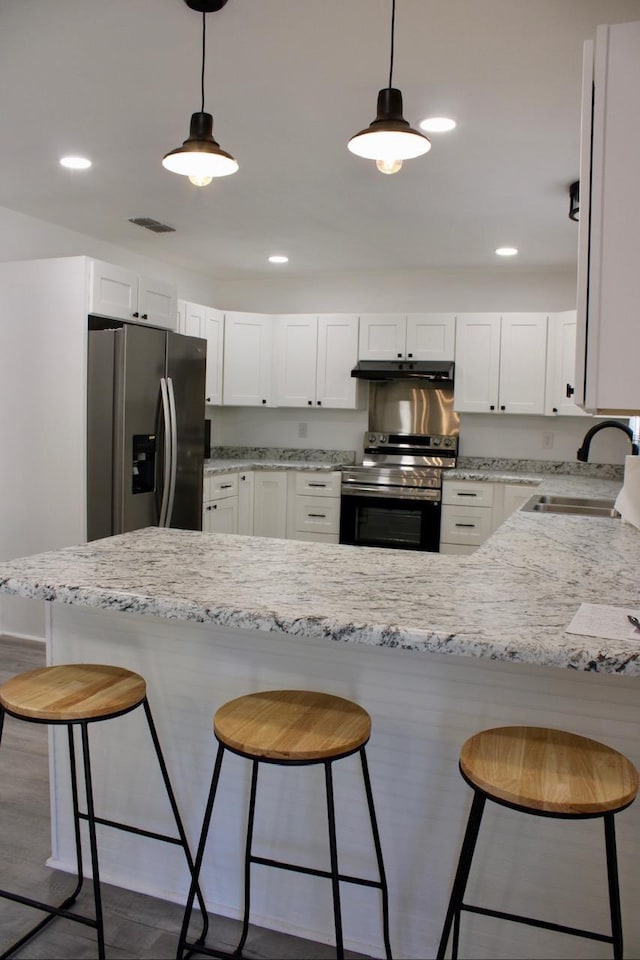 kitchen featuring sink, light stone countertops, appliances with stainless steel finishes, decorative light fixtures, and white cabinetry