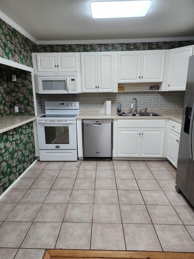 kitchen featuring sink, light tile patterned floors, appliances with stainless steel finishes, white cabinetry, and ornamental molding