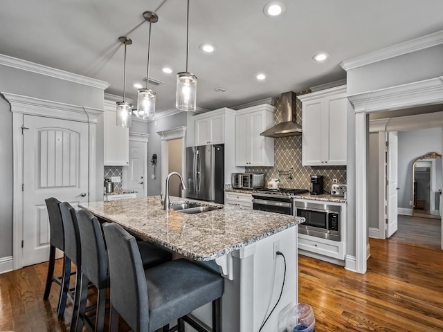 kitchen featuring white cabinetry, appliances with stainless steel finishes, a kitchen island with sink, and wall chimney range hood