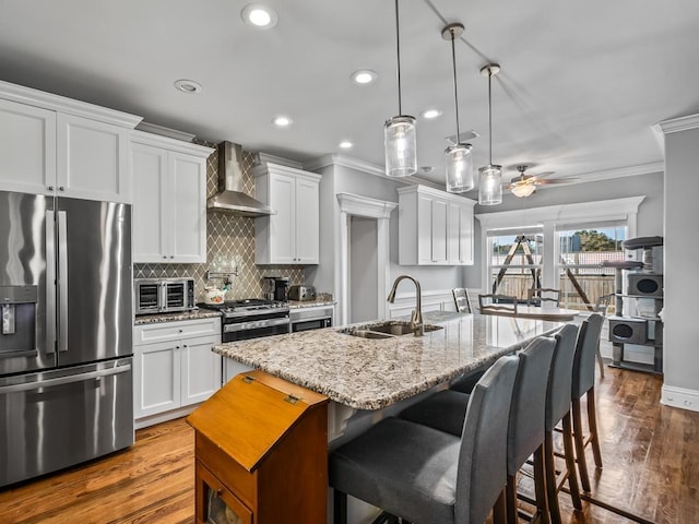 kitchen featuring decorative light fixtures, sink, white cabinets, stainless steel appliances, and wall chimney range hood