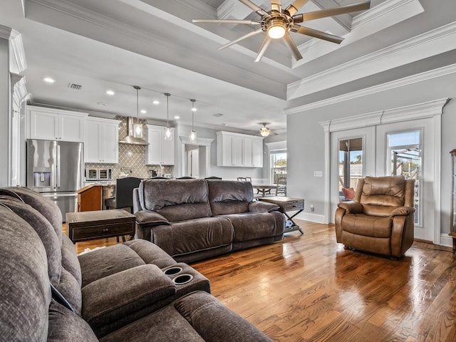 living room featuring ornamental molding, wood-type flooring, ceiling fan, and a tray ceiling