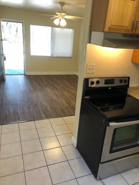 kitchen featuring light tile patterned floors, under cabinet range hood, electric range, a ceiling fan, and brown cabinetry