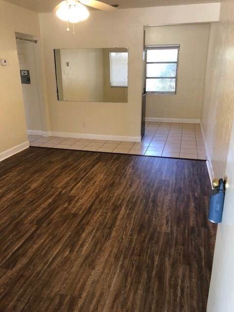 empty room featuring dark wood-type flooring, a ceiling fan, and baseboards