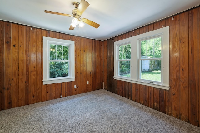 carpeted spare room with wood walls and a ceiling fan