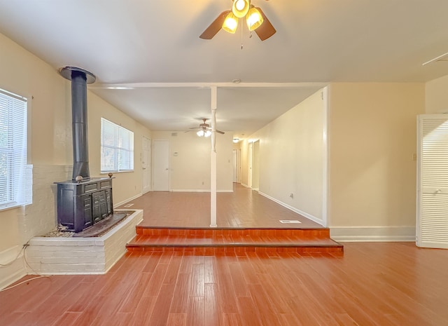 unfurnished living room with baseboards, ceiling fan, wood finished floors, and a wood stove