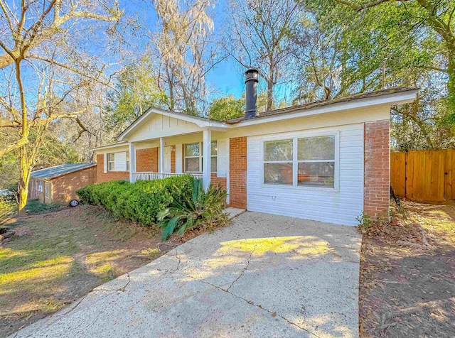 view of front of property featuring concrete driveway, fence, a porch, and brick siding