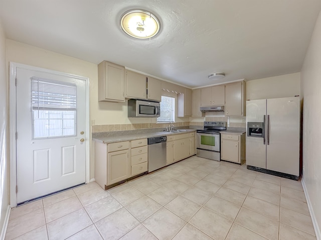 kitchen featuring cream cabinetry, a sink, light countertops, under cabinet range hood, and appliances with stainless steel finishes