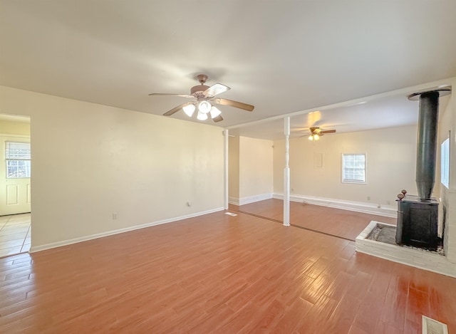 unfurnished living room with ceiling fan, visible vents, baseboards, a wood stove, and light wood-type flooring