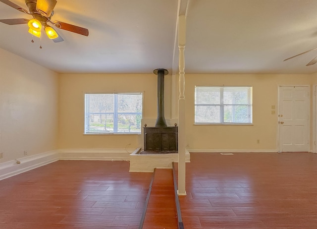 unfurnished living room featuring baseboards, ceiling fan, dark wood-style flooring, and a wood stove