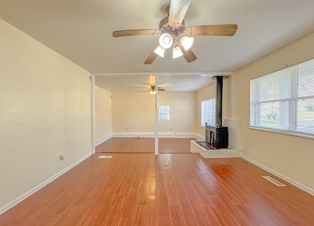 unfurnished living room featuring light wood-style flooring, visible vents, baseboards, and a wood stove