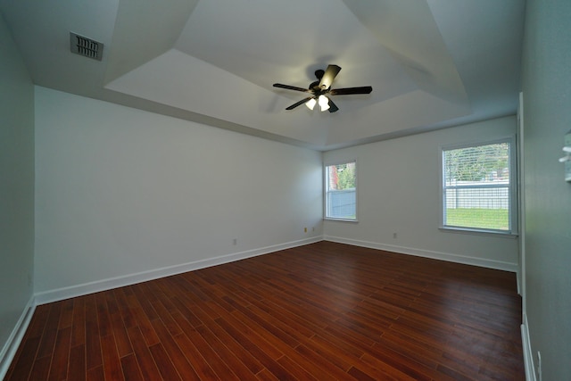 unfurnished room with ceiling fan, a raised ceiling, and dark wood-type flooring