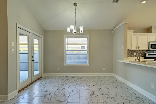 unfurnished dining area with lofted ceiling, sink, french doors, and a notable chandelier