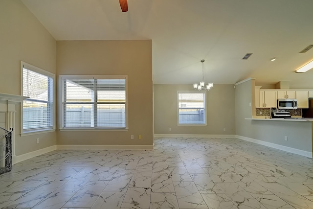 unfurnished living room featuring ceiling fan with notable chandelier, a wealth of natural light, and vaulted ceiling