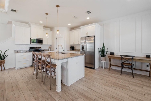 kitchen featuring a kitchen bar, visible vents, light wood-style flooring, a sink, and stainless steel appliances