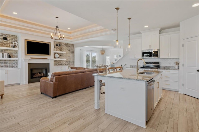 kitchen with light wood-type flooring, a sink, a tray ceiling, appliances with stainless steel finishes, and a breakfast bar area