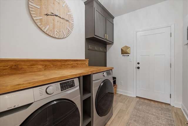 clothes washing area featuring baseboards, cabinet space, light wood-style floors, and washer and clothes dryer