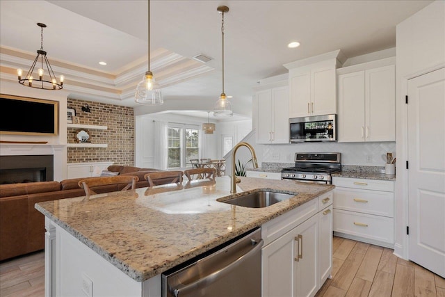 kitchen featuring open floor plan, a tray ceiling, light wood-style flooring, appliances with stainless steel finishes, and a sink