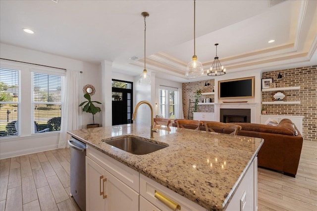 kitchen with a sink, a raised ceiling, light wood-style floors, and dishwasher