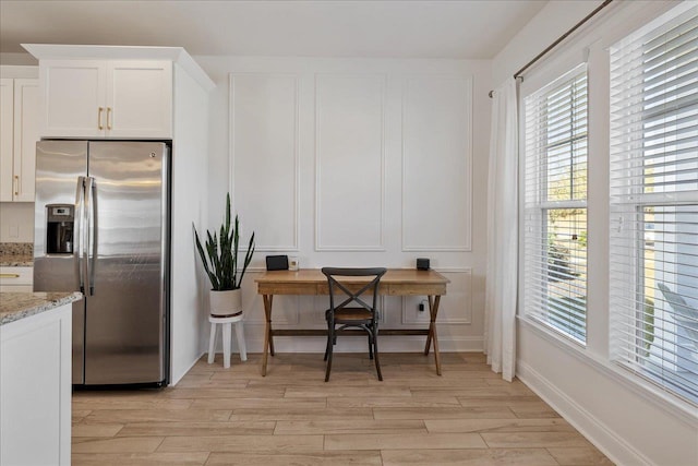 kitchen featuring stainless steel fridge, white cabinets, light wood-style floors, and light stone countertops