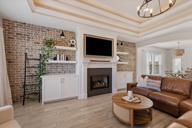 living room with brick wall, ornamental molding, light wood-style flooring, a fireplace, and a raised ceiling