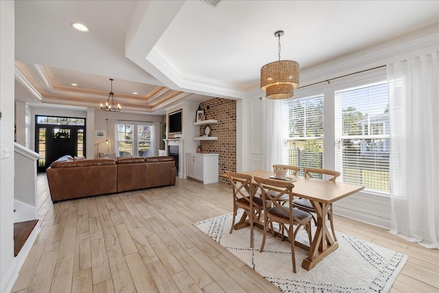 dining area with an inviting chandelier, a fireplace, ornamental molding, a raised ceiling, and light wood-type flooring
